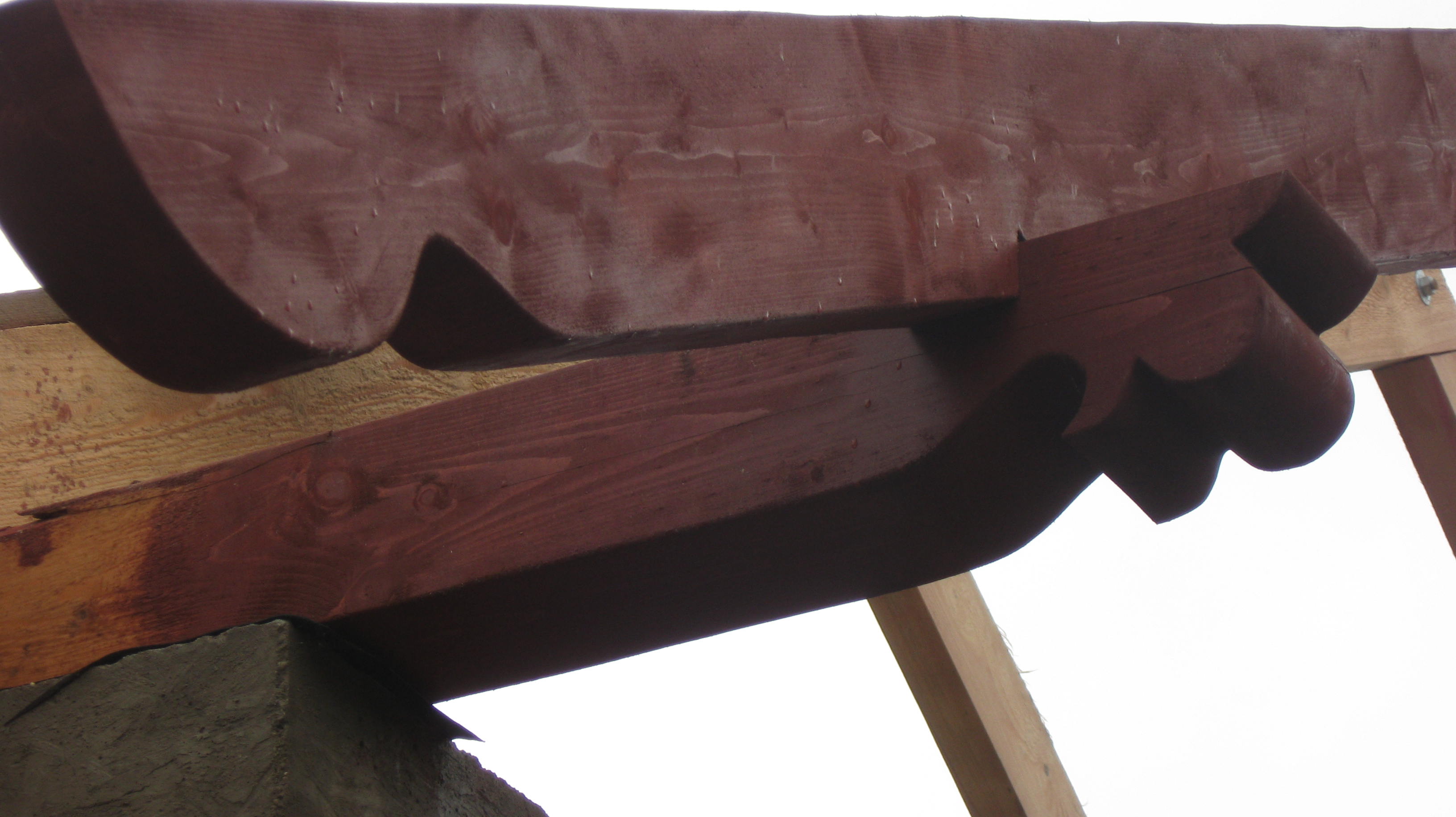 Drewniana konstrukcja dachu z ozdobnymi wykończeniami, pomalowana na brązowo, widoczna z dołu.